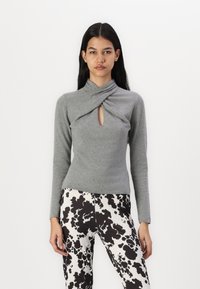 Gray long-sleeve top with a twisted collar and a front cutout, paired with black and white spotted patterned pants; soft knit material.