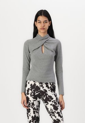 Maglietta grigia a maniche lunghe con colletto attorcigliato e apertura frontale, abbinata a pantaloni a pois bianchi e neri; materiale in maglia morbida.