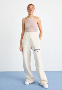 Světle béžový halter top spárovaný s krémovými širokými kalhotami, které mají výrazné vyšívané logo Nike, nošený s bílými teniskami.