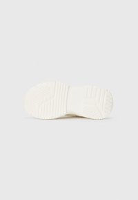 Semelle de chaussure de sport blanche avec des motifs de grip texturés, une section centrale lisse et un bout arrondi, présentant une semelle prononcée et des détails de marque.