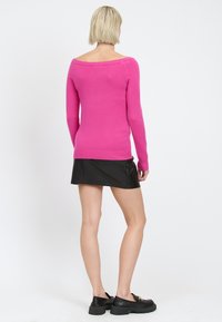 Maglione aderente rosa con maniche lunghe e scollatura off-the-shoulder. Abbinato a una mini gonna in pelle nera e scarpe nere chunky.