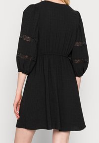 Vestido negro con tejido texturizado, mangas abullonadas con inserciones de encaje y cintura elástica. Falda acampanada que llega a medio muslo.