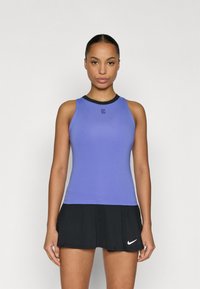 Μωβ αθλητική μπλούζα χωρίς μανίκια με μαύρο ντεκολτέ, με μικρό λογότυπο στο στήθος. Συνδυάζεται με μαύρη πλισέ φούστα τένις.