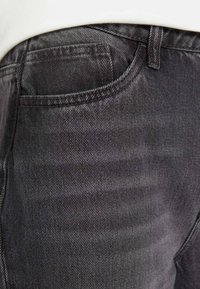 Dark gray denim jeans with a subtle texture, featuring a side pocket and belt loops. Focus on the fabric's diagonal weave pattern.