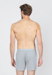 Grijze katoenen boxershorts met een elastische tailleband, met een gladde textuur en een casual pasvorm, getoond vanuit een achteraanzicht.