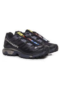 Chaussures de trail running Salomon noires avec une tige en maille texturée, des accents réfléchissants et une semelle extérieure robuste. Dotées d'un système de laçage rapide.