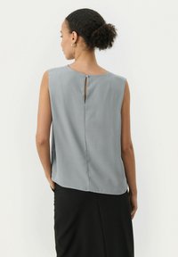 Sleeveless, light gray blouse featuring a keyhole back closure and smooth texture, paired with a black skirt, showcasing a relaxed fit.