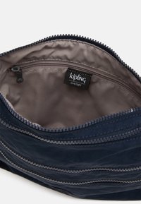Navyblå Kipling taske indvendig, med en glat, struktureret foring, der har en lynlås lomme og et mærkater, der viser en holdbar konstruktion.