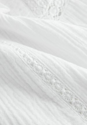 Weiche weiße Stofffalten mit strukturierten, gewebten und spitzenähnlichen Stickmustern, die zarte horizontale Streifen bilden.