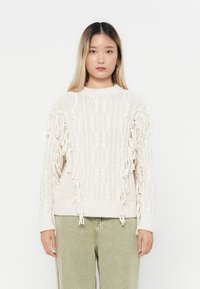 Cremfarbener Strickpullover mit einem Zopfmuster und Fransenverzierungen an den Ärmeln. Gerippte Bündchen und Saum sorgen für Stabilität.