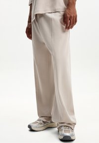 Light beige wide-leg pants made of soft fabric, featuring a smooth texture and subtle stitching. Paired with light athletic shoes with mesh detail.