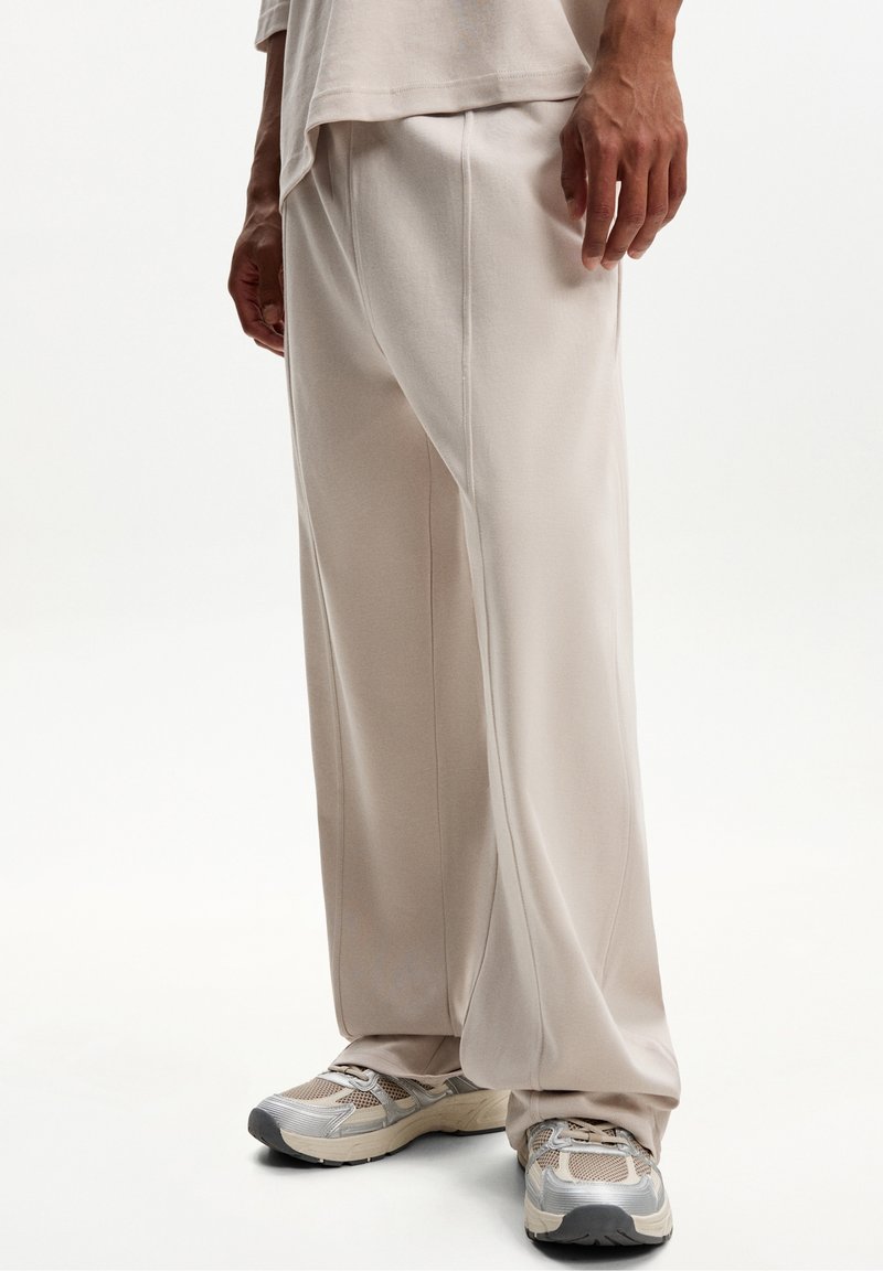 Light beige wide-leg pants made of soft fabric, featuring a smooth texture and subtle stitching. Paired with light athletic shoes with mesh detail.