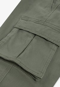 Ελιόχρωμο cargo παντελόνι από υφασμάτινο υλικό με υφή, μεγάλο μπροστινό τσέπη και ορατές ραφές.