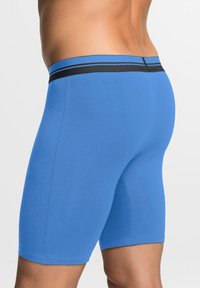 Boxers bleus en mélange de coton, dotés d'une taille élastique noire avec deux rayures bleues, texture lisse et design ajusté.