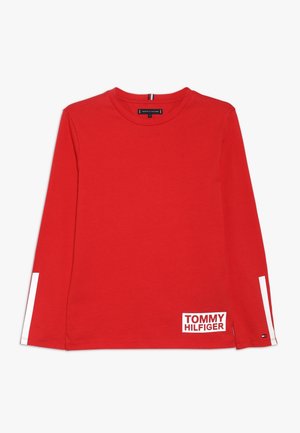 Czerwona koszula z długim rękawem wykonana z bawełny, z białymi akcentami na rękawach i prostokątną metką z logo "TOMMY HILFIGER" na dolnym brzegu.