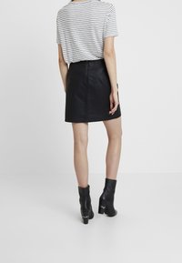 Svart fusk läder mini kjol med en strukturerad yta, i kombination med en grå och vit randig t-shirt och svarta ankelstövlar.