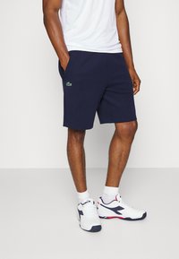 Navy shorts made of cotton blend, featuring side pockets and an embroidered green logo. Paired with white athletic shoes and socks.