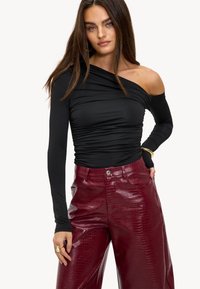 Zwarte off-the-shoulder top met lange mouwen en geplooide textuur, gecombineerd met glanzende bordeauxrode nep-krokodillenleren wijde broek.