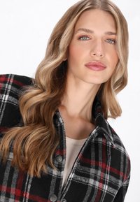 Chemise en flanelle à carreaux noire, rouge et blanche avec un col et des boutons. Texture douce, avec un motif à carreaux classique.