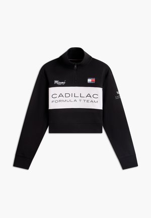 Μαύρο φούτερ με φερμουάρ στο τέταρτο, με λευκή ταινία που αναγράφει «Cadillac Formula 1 Team», κέντημα Μαϊάμι και λογότυπο Tommy Hilfiger στο στήθος.