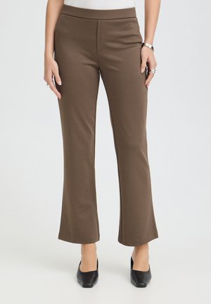 Braune gerade geschnittene Hosen getragen mit schwarzen spitzen Pumps, sichtbar von der Taille bis zu den Füßen vor einem einfarbigen hellen Hintergrund.