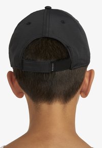 Černá čepice s prohnutým kšiltem, nastavitelným páskem vzadu a texturovanou tkaninou. Nad páskem je štítek s logem.