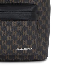 Fekete és barna geometrikus mintázatú műbőr táska, elülső zsebbel és alul fehér "KARL LAGERFELD" logóval. Simaszerű textúrájú.