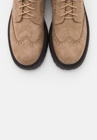 Ljusbruna mockabrogueskor med perforerade detaljer, snörning och tjock svart gummisula. Sedd uppifrån.