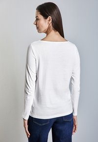 Weißes Langarmoberteil mit einem Bootsausschnitt, glatter Textur und lockerer Passform, kombiniert mit dunklen Jeans. Einfaches und vielseitiges Design.
