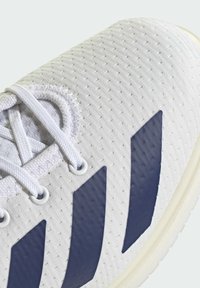 White athletic shoe featuring a textured mesh upper, three navy blue stripes on the side, and white laces threaded through circular eyelets.