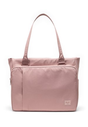 Sac cabas rose doux avec de longues poignées, poche zippée à l'avant et petite étiquette de marque rectangulaire en bas à droite.