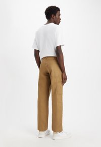 Pantalones cargo color caqui con múltiples bolsillos, material de algodón y corte relajado. Combinados con una camiseta de manga corta blanca y zapatillas blancas.