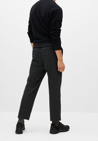 Pantaloni in lana grigia con design a gamba dritta, caratterizzati da due tasche posteriori e una finitura testurizzata, abbinati a un maglione nero e sneakers.