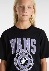 Černé bavlněné tričko s velkým fialovým a bílým grafickým designem "VANS" a kruhovým logem s textem "WAFFLE WORKS". Krátké rukávy.