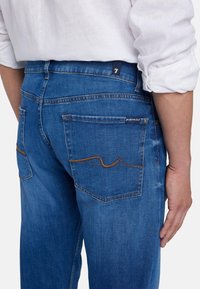 Jeans in denim blu con taglio dritto, dotati di due tasche posteriori, dettagli con cuciture arancioni e una etichetta sulla vita.