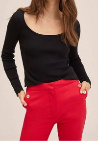Haut noir côtelé à manches longues avec un col carré, associé à un pantalon rouge taille haute avec deux boutons décoratifs à la taille.