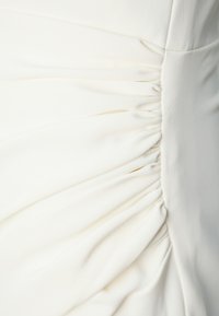 Tissu cream avec texture plissée et fronces, présentant une surface lisse et un drapé doux, créant un design fluide sur le vêtement.