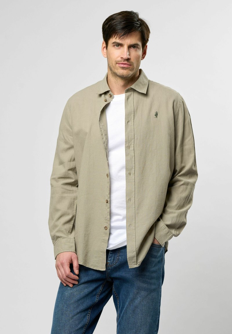 Camisa de botón color beige claro con un corte relajado, de mangas largas y una textura sutil; combinada con una camiseta blanca y jeans azules.