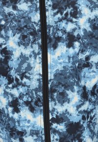 Giacca multicolore con un motivo astratto blu e nero, caratterizzata da una texture liscia e una zip frontale che corre nel mezzo.