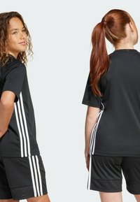 Conjunto de camiseta y pantalones cortos deportivos negros con franjas blancas en los laterales. De manga corta, tejido suave y corte relajado.
