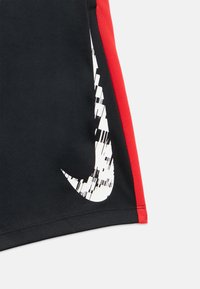 Fekete sportnadrág piros oldalsó panellel. Nagy, fehér Nike pipa logóval, pixeles dizájnnal. Sima, rugalmas anyagból készült.