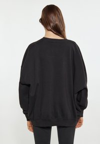 Felpa nera oversized con spalle scese, polsini e orlo a coste. Realizzata in tessuto morbido con una vestibilità comoda e senza motivi visibili.