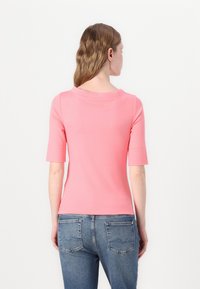 Roze top met korte mouwen en een ronde halslijn, gemaakt van gladde stof. De achterkant heeft een subtiele naaddetail. Gepaard met blauwe denim jeans.