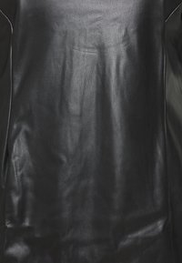 Vêtement en cuir noir avec une texture lisse, présentant une finition légèrement brillante et des détails de couture minimaux sur les côtés.