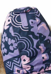 Mochila colorida con una base azul oscura, con intrincados patrones florales y geométricos en púrpura y rosa. Incluye una asa de tela.