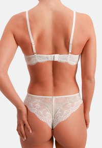 Weißer Spitzen-BH und passende Pantys mit aufwendigen Blumenmustern, verstellbaren Trägern und einem Hakenverschluss auf der Rückseite.