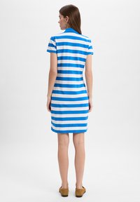 Korte mouwen gestreepte jurk in blauw en wit, met een kraag en van gemiddelde dijlengte. Glad, lichtgewicht stof. Bruine instap schoenen.