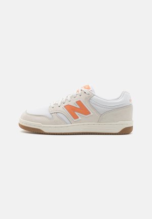Sneaker bassa bianca e beige con logo "N" arancione, chiusura con lacci e suola in gomma marrone, mostrata su uno sfondo bianco.