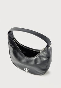 Μαύρη δερμάτινη τσάντα ώμου με ασημένιο φερμουάρ, μονή ιμάντα και ασημένιο λογότυπο «cK» στο μπροστινό μέρος, ελαφρώς ανοιχτή αποκαλύπτοντας την εσωτερική επένδυση.