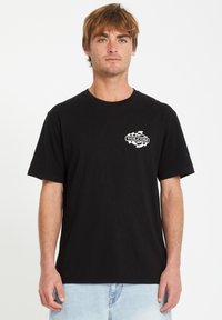 Schwarzes Baumwoll-T-Shirt mit einem weißen Grafiklogo auf der linken Brustseite und kurzen Ärmeln. Rundhalsausschnitt, lässige Passform.